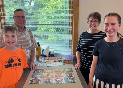 Four people stand around a table with a completed jigsaw puzzle.