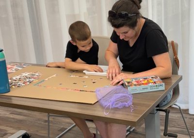 A woman and boy working on a jigsaw puzzle at a table with a water bottle and puzzle box.