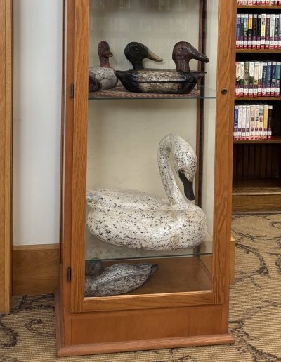 A wooden cabinet with glass doors displaying duck and swan decoys.