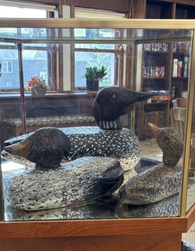 Three carved wooden duck figures displayed in a glass case with wooden and brass framing.