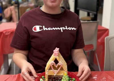 Person holding a gingerbread house decorated with candy on a red plate.