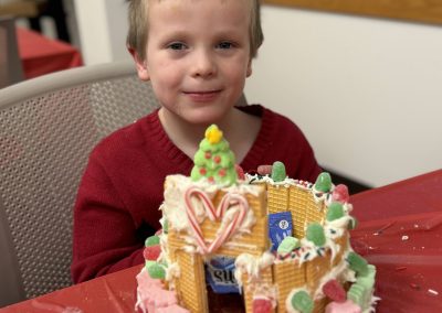 Child smiling in front of a decorated gingerbread house with waffle cookies and colorful candies.