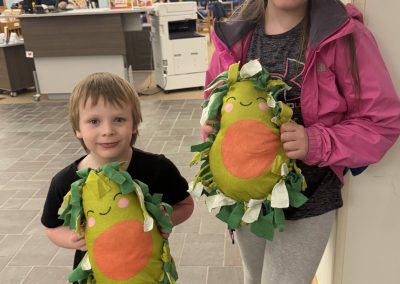 Two children holding their finished avocado pillows in a library setting.